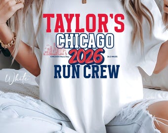 May include: A white short-sleeved t-shirt featuring red and navy blue text that reads Taylor's Chicago 2026 Run Crew. The design includes a small red outline of the Chicago skyline, the text Chicago Race Day, and the measurement 26.2 miles.