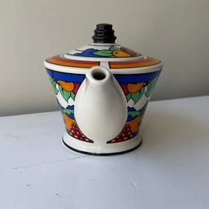 Puede incluir: Una tetera de cer&aacute;mica vintage con un colorido dise&ntilde;o de frutas y hojas. La tetera tiene un cuerpo blanco con una base y un asa negras. La tapa tiene un pomo negro y una banda de colores del arco&iacute;ris.