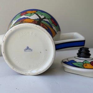 Puede incluir: Una tetera Sadler vintage con un colorido dise&ntilde;o de frutas y &aacute;rboles. La tetera presenta un cuerpo blanco con un asa negra y una franja azul. La tapa est&aacute; a un lado, mostrando el dise&ntilde;o de frutas. La parte inferior de la tetera dice "MADE IN ENGLAND".