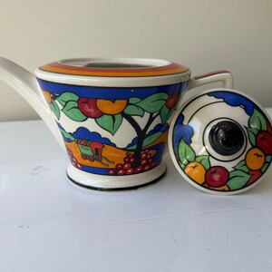 Puede incluir: Tetera de cer&aacute;mica vintage con tapa. La tetera tiene una base blanca con un borde negro, un pico y un asa. El dise&ntilde;o presenta un paisaje con frutas y &aacute;rboles. La tapa tiene un pomo negro y un patr&oacute;n a juego de frutas y hojas.