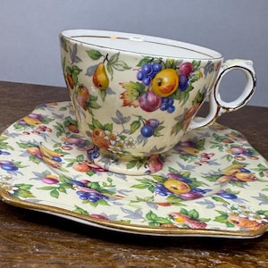Puede incluir: Un juego de taza y platillo vintage con un patrón floral que presenta una variedad de frutas, incluyendo peras, manzanas y uvas. El juego está decorado con ribetes dorados.