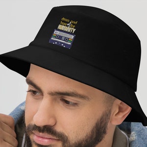 Op de afbeelding: Zwarte bucket hat met een cassetteband-afbeelding en de tekst "drum and bass for humanity".