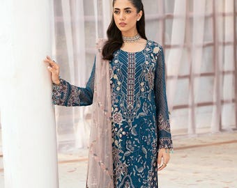 Puede incluir: Un vestido largo de manga larga azul turquesa con intrincados bordados florales y un dupatta a juego. El dupatta es una tela transparente con un diseño rosa y dorado. El vestido tiene un escote redondo y un corpiño ajustado. El vestido se combina con pantalones azul turquesa.