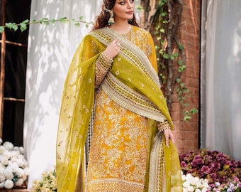 May include: A woman wearing a yellow and gold embroidered dress with a matching dupatta. The dupatta is a sheer green fabric with gold embroidery. The dress has a long-sleeved design and is paired with yellow pants.