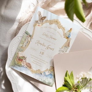 Może przedstawiać: Prostokątne zaproszenie na baby shower ze złotą, ozdobną ramką oraz akwarelowymi ilustracjami jelenia, sowy i dziewczynki w niebieskiej sukience. Tekst zawiera napis A NEW CHAPTER BEGINS, Baby Shower, Amelia Jones, 18 sierpnia 2023 oraz inne dane.