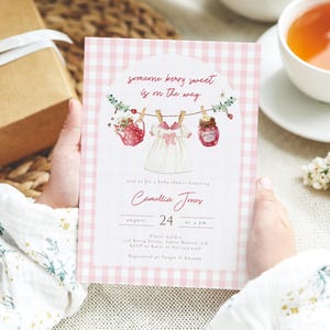 Puede incluir: Una invitación a un baby shower con un fondo de patrón de cuadros rosas. La invitación presenta el texto "someone berry sweet is on the way" e ilustraciones de una tetera, un vestido de bebé y un tarro de mermelada. La invitación es para Camellia Jones.