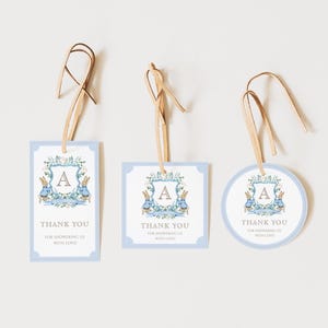 May include: Three baby shower gift tags in different shapes: rectangular, square, and circular. Each tag has a light blue border and features a floral wreath with two rabbits and the letter "A". The tags read "Thank You".