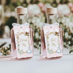 May include: Two glass bottles filled with a pink liquid, each with a beige cap. The bottles have tags with an Alice in Wonderland theme, including the phrases "Drink Me" and "Eat Me" within a decorative frame. The tags are pink and gold.