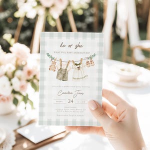 Puede incluir: Invitación a una fiesta de revelación de género, sostenida por una mano. La invitación presenta un patrón de cuadros verdes claros y blancos. El texto dice "he or she, what will baby Anderson be?" e incluye ilustraciones de ropa de bebé.