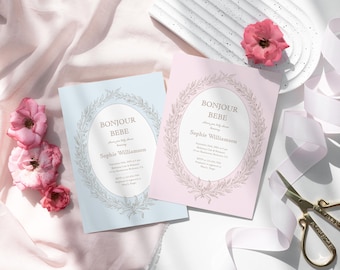Puede incluir: Dos tarjetas de invitación rectangulares para baby shower en azul claro y rosa suave. Cada tarjeta presenta un marco ovalado central con un diseño de corona botánica, el texto "BONJOUR BEBE" y el nombre "Sophie Williamson" en fuente serif.