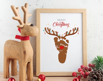 Può includere: Una stampa incorniciata di una renna realizzata con un'impronta di piede marrone. La renna ha il naso rosso ed è decorata con luci colorate. La stampa dice "Buon Natale".