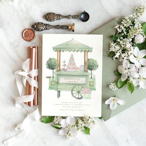 Puede incluir: Una tarjeta de invitación con una ilustración en acuarela de un carrito de postres verde, con una torre de macarons y detalles florales. La tarjeta incluye el texto "CAMELIA Sweet One" y detalles del evento. Sellos de cera decorativos, cintas y flores acompañan la tarjeta.