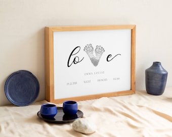 May include: A framed print with a silver footprint design in the shape of a heart. The print says "love" with the footprints forming the "o". The print also includes the name "Emma Louise", the date "09.22.20XX", the time "11:12 AM", and the length "19.8 inches".