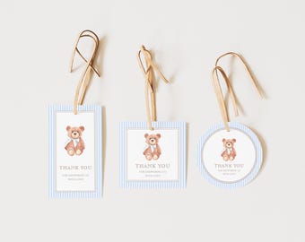May include: Three baby shower gift tags with a teddy bear illustration. The tags have a blue and white striped background and a brown ribbon. The text "THANK YOU FOR SHOWERING US WITH LOVE" is printed on the tags.