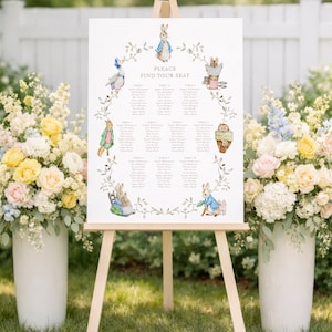 May include: A wooden easel supports a wedding seating plan with the text "PLEASE FIND YOUR SEAT". The chart features illustrations of Peter Rabbit characters and a floral wreath design. Two large white vases with colourful flowers flank the easel.