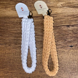 May include: Two crocheted keychains with metal key rings. The keychain on the left is white and the keychain on the right is tan.