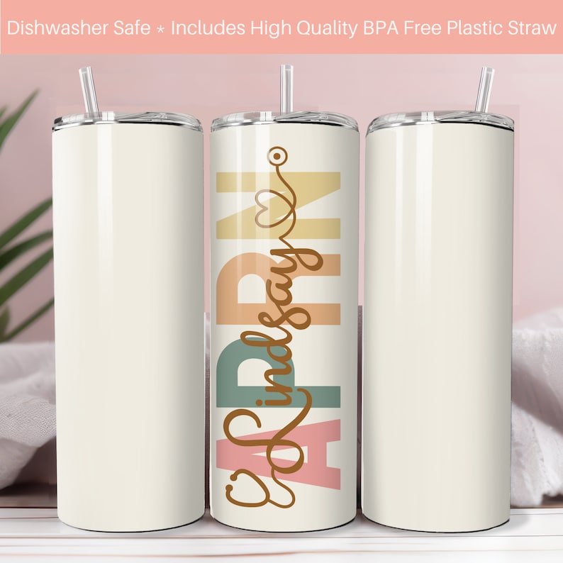May include: Three stainless steel tumblers with a white background. The center tumbler has the text "RN" in large letters with a stethoscope and heart symbol. The text "Lindsay" is written in cursive below the letters. The tumblers are on a white wooden surface.