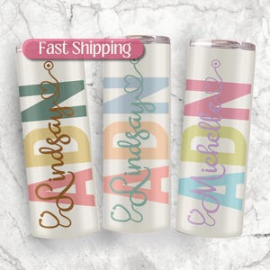 May include: Three white stainless steel tumblers with colorful text that reads "RN" and a stethoscope symbol. The names "Lindsay" and "Michelle" are written in cursive on the tumblers.