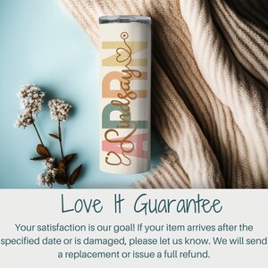 May include: A white stainless steel tumbler with a colorful design featuring the name "Lindsay" and a heart. The tumbler is on a light blue background with a beige knitted blanket.