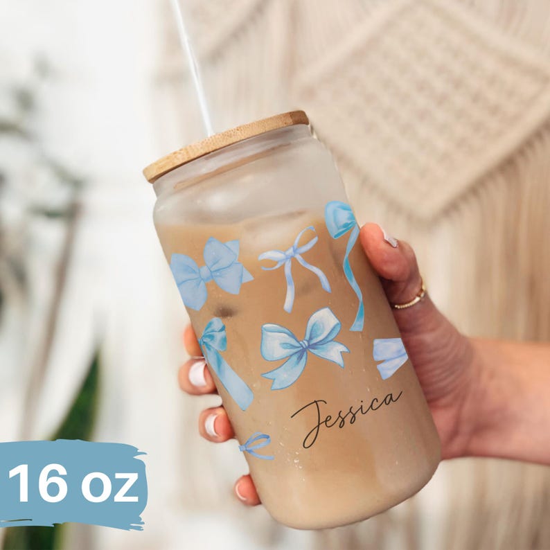 May include: A 16 ounce glass tumbler with a bamboo lid and a straw. The tumbler has a design of blue bows and the name "Jessica" written on it.