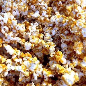 May include: Close-up of caramel popcorn. The popcorn kernels are coated in a glossy, golden-brown caramel. The image shows a dense pile of popcorn, with the caramel creating a textured, sweet treat.