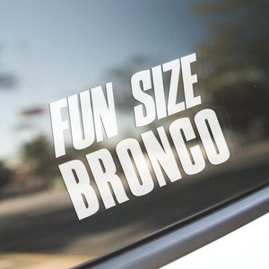 May include: White vinyl sticker displaying the text "FUN SIZE BRONCO" in a bold, sans-serif font. The sticker is affixed to a dark surface, with a blurred background suggesting an outdoor setting.