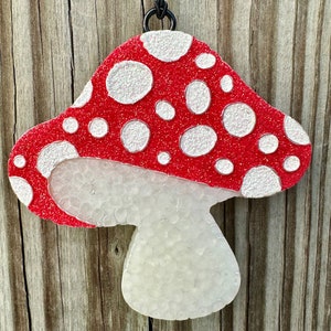 May include: A red and white mushroom ornament with white polka dots. The mushroom is hanging from a black string.