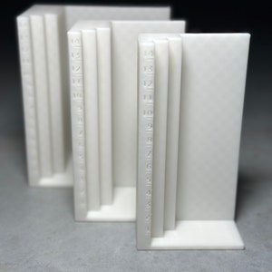 May include: Three white plastic rulers with numbers 1 through 14 marked on the side. The rulers are stacked on top of each other.