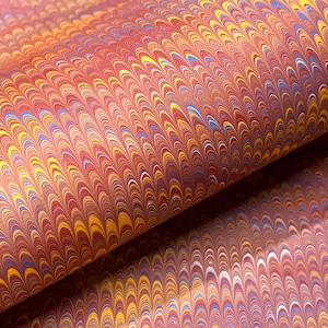 Könnte beinhalten: Ein Blatt Papier mit einem sich wiederholenden Marmormuster mit bogenförmigen, federartigen Formen in den Farben Rot, Orange, Gelb, Blau und Weiß. Das Design zeigt eine dichte, symmetrische Anordnung geschwungener Linien mit strukturierter Optik.