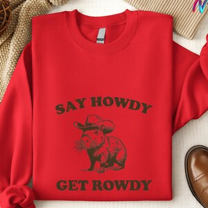 May include: Red sweatshirt with the text "Say Howdy Get Rowdy" in brown lettering. A cartoon capybara wearing a cowboy hat is in the center of the text.