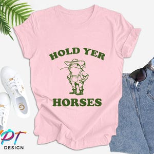 May include: Pink t-shirt with a green frog wearing a hat and the text "HOLD YER HORSES".