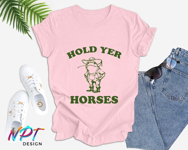 May include: Pink t-shirt with a green frog wearing a hat and the text "HOLD YER HORSES".