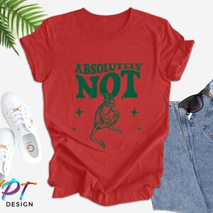 Puede incluir: Camiseta roja con un gr&aacute;fico de rana verde y el texto "ABSOLUTELY NOT" en letras verdes.