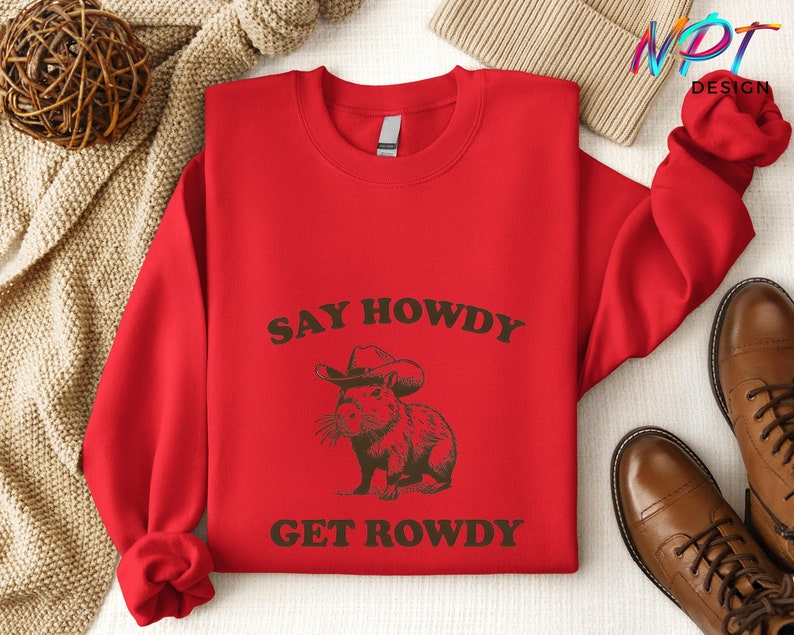 May include: Red sweatshirt with the text "Say Howdy Get Rowdy" in brown lettering. A cartoon capybara wearing a cowboy hat is in the center of the text.