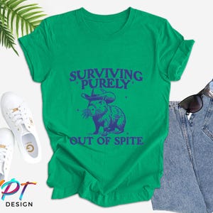 May include: Green t-shirt with a blue graphic of a capybara wearing a witch hat and the text "Surviving Purely Out of Spite".