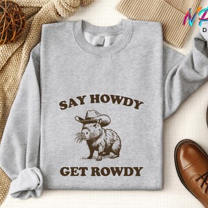 May include: A gray sweatshirt with the text "Say Howdy Get Rowdy" and a cartoon capybara wearing a cowboy hat.