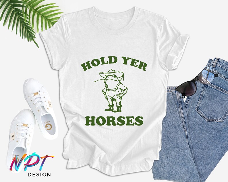 May include: White t-shirt with green text that says "Hold Yer Horses" and a cartoon frog wearing a hat and overalls.