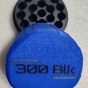 May include: A blue, textured, circular object with the text "300 BLK" in gray and black. A black, circular object with multiple holes is behind the blue object. The objects appear to be made of plastic.