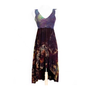 Pode incluir: Um vestido maxi tie-dye com corpete de crochê. O vestido apresenta um decote em V e uma bainha assimétrica. O corpete é uma mistura de roxo, verde e azul. A saia é uma mistura de marrom, roxo e bege.