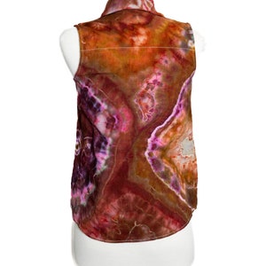 May include: A sleeveless shirt with a tie-dye pattern in shades of orange, brown, pink, and purple. The shirt has a button-up collar and a relaxed fit.