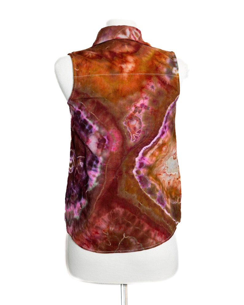 May include: A sleeveless shirt with a tie-dye pattern in shades of orange, brown, pink, and purple. The shirt has a button-up collar and a relaxed fit.