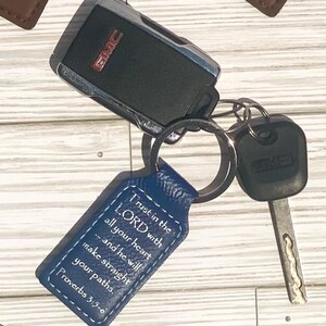 May include: A set of keys with a blue leather keychain. The keychain has the text "Trust in the LORD with all your heart...and he will make straight your paths. Proverbs 3:5-6". A black GMC key fob and a metal key are also attached.