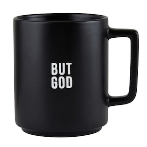May include: Black ceramic mug with a square handle. The mug features the white text "BUT GOD" on the front. The mug has a simple, modern design.