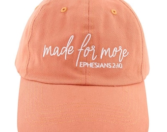 May include: A peach-colored baseball cap with a curved brim. The cap features the white script text "made for more" and the text "Ephesians 2:10". The cap has a button on top and adjustable strap.