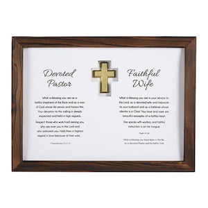 May include: A framed wall art piece with a dark brown wooden frame. The artwork features the words "Devoted Pastor" and "Faithful Wife" with related text, and a gold-colored cross in the center.