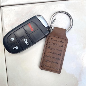 May include: A black car key fob with silver accents and a brown leather keychain. The keychain has a silver ring and features the text "Trust in the LORD with all your heart... Proverbs 3:5-6".