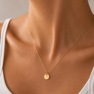 Peut inclure: Un collier doré délicat composé d'une chaîne fine et d'un petit pendentif circulaire plat. Le pendentif est suspendu au centre de la chaîne qui repose sur la zone de la clavicule, mettant en valeur une finition métallique simple et polie.