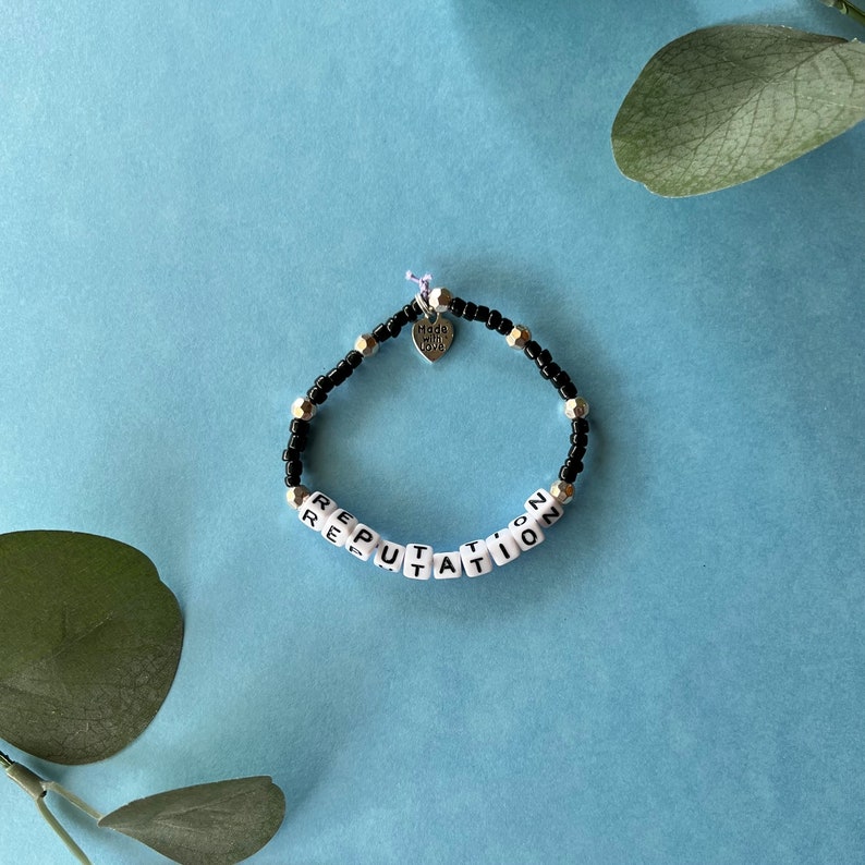 Pode incluir: Uma pulseira de contas com a palavra "REPUTATION" escrita em contas de letras brancas. A pulseira tamb&eacute;m apresenta contas pretas e prateadas, e um pequeno pingente de cora&ccedil;&atilde;o que diz "Made with Love".