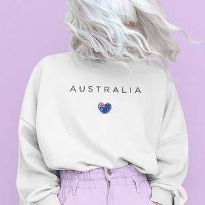May include: A white sweatshirt with the word "AUSTRALIA" printed on the front, and a small heart with the Australian flag inside. The model is wearing light purple pants.