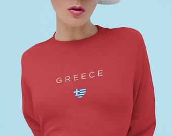 Peut inclure: Sweat-shirt rouge avec le mot "GREECE" en blanc et un cœur avec le drapeau grec à l'intérieur.
